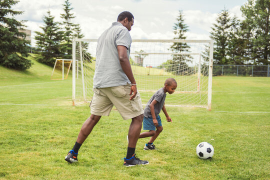 father with son playing football or soccer outside on field