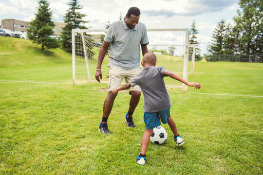 father with son playing football or soccer outside on field