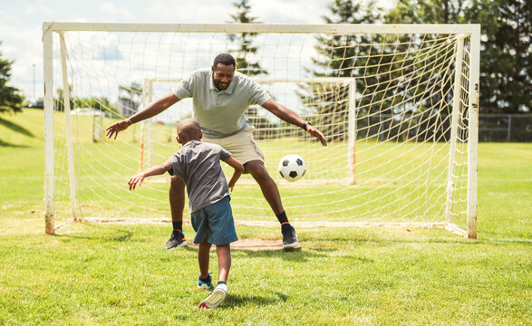 father with son playing football or soccer outside on field