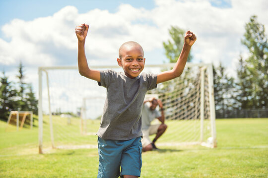 father with son playing football or soccer outside on field