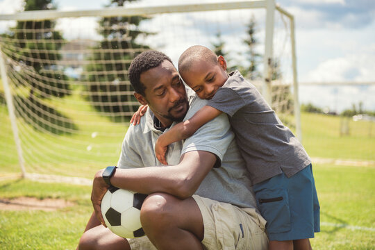father with son playing football or soccer outside on field