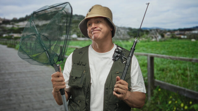 Man holding fishing net and rod, pouting lips and gripping pole on a wooden boardwalk forest; frustration patience.