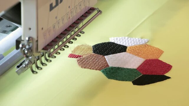An automatic Juki embroidery machine artfully stitches a vibrant, intricate geometric pattern onto a bright yellow fabric. This showcases modern textile manufacturing.