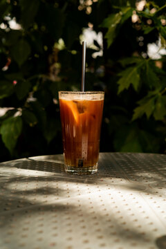 Iced espresso tonic glass on a metal table in a sunlit garden