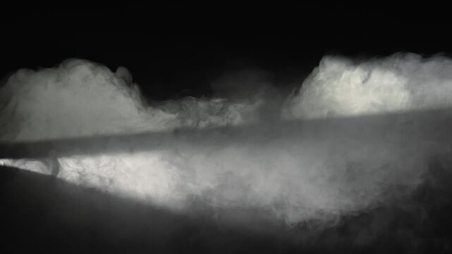 A white spotlight crosses dense smoke on a black background. Concept of overlay real effect, theater, concert, cinema, event, advertising, presentation, backdrop, and dramatic design.