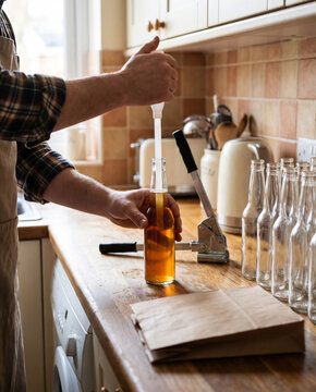 Hands filling a beer bottle with a bottling wand beside a capper and clean bottles