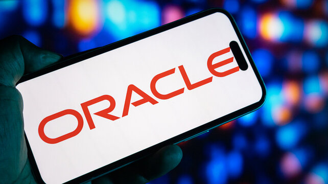 Smartphone screen showing oracle logo held by hand against colorful bokeh background in dark setting indoors at night.