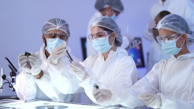 Cleanroom worker holds up a small device for inspection as masked teammates examine it closely during a quality check in a sterile controlled research laboratory