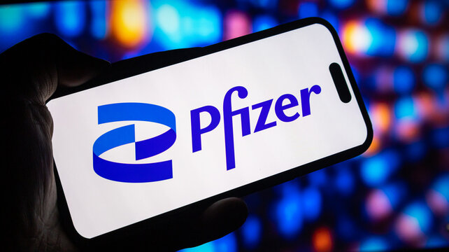 Pfizer corporate brand logo displayed on modern smartphone screen held in hand against blurred digital monitor backdrop now.