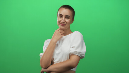 Obraz premium Woman with short hair touching her neck and smiling, wearing white puff sleeve top and arms folded, posed against green studio backdrop; confidence.