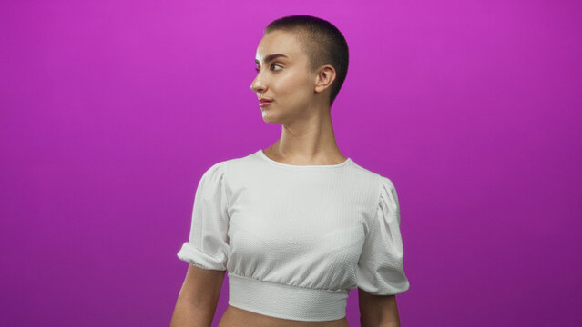 Woman with buzzcut facing camera, bare midriff visible and turning head in subtle poses against purple studio backdrop; confidence.