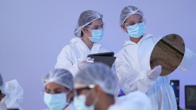 Engineer displays the rainbow diffraction of a silicon wafer while a colleague holds a tablet during a semiconductor quality inspection in a sterile hitech cleanroom