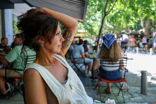 Woman relaxing at an outdoor cafe beneath leafy trees in Greece, capturing everyday travel moments, local culture, and a vibrant urban atmosphere.