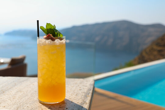 Orange cocktail beside an infinity pool overlooking the Santorini caldera, with sweeping views of the Aegean Sea and volcanic cliffs in Greece.