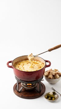 Delicious Cheese Fondue with Bread Cubes and Pickles Served in a Red Pot on a White Background