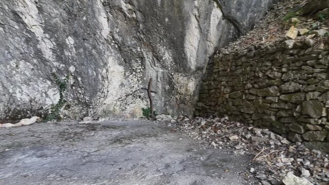 Area rocciosa con pareti in pietra naturale, terreno irregolare con foglie secche e piccoli arbusti alla base