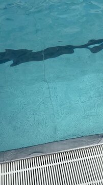 Water surface in blue swimming pool close up. Minimalistic background with waving water and texture of swimming pool bottom tiles. Sport, rest, vacation and activity