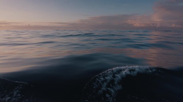 Low-angle view of gentle ocean waves reflecting pastel twilight colors beneath a cloudy sky