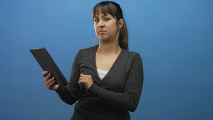 Woman holding tablet, tapping screen with one finger, grimacing then covering her mouth while reading in a blue studio  disgust reaction. © Krakenimages.com