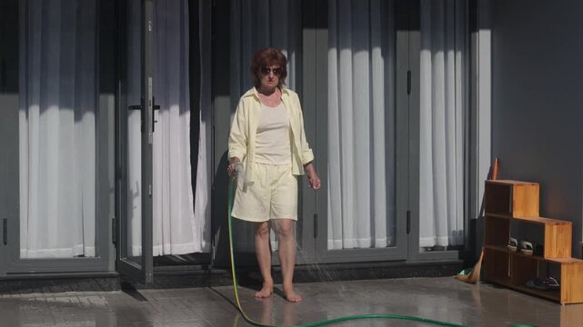 Homeowner rinses patio and entrance with water, creating fresh and tidy outdoor space. Property care reflects responsible home maintenance, making property care valuable for residential living.