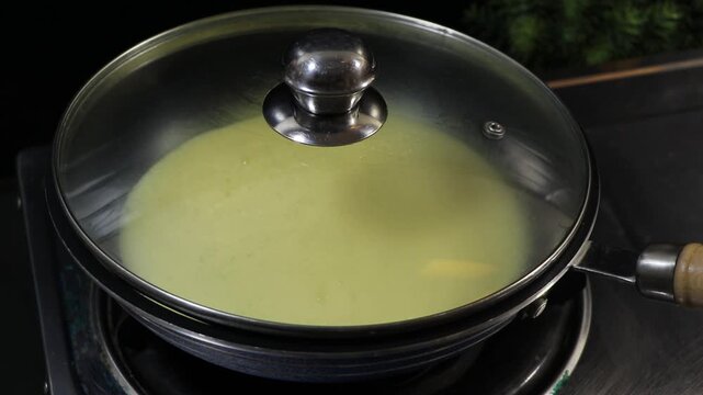 Covering a frying pan with a glass lid to steam cook an egg mixture
