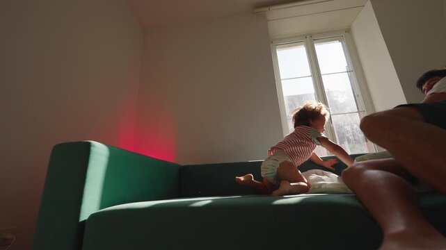 Father carefully diving onto sofa before toddler follows at home, playful family sequence expressing trust, guidance, bonding and shared adventure