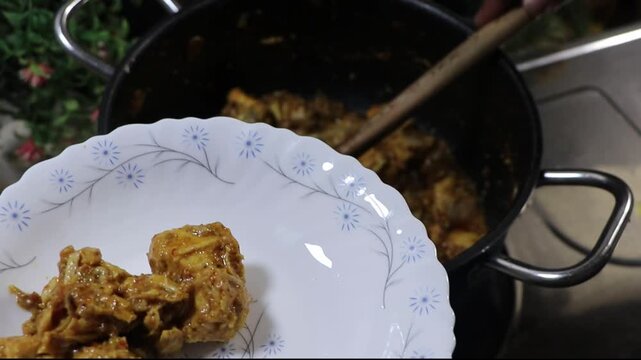 Person serving delicious chicken karahi from a pot onto a white plate
