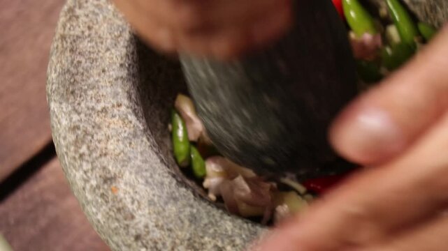 Close-up of crushing ingredients with a granite pestle and mortar to make traditional Nam Phrik Kapi in Bangkok, Thailand.