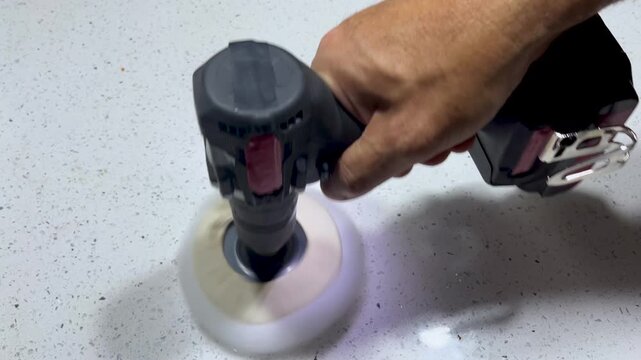 Worker's hand polishing a kitchen countertop with a cordless electric sander, achieving a smooth and shiny surface through careful craftsmanship and finishing work