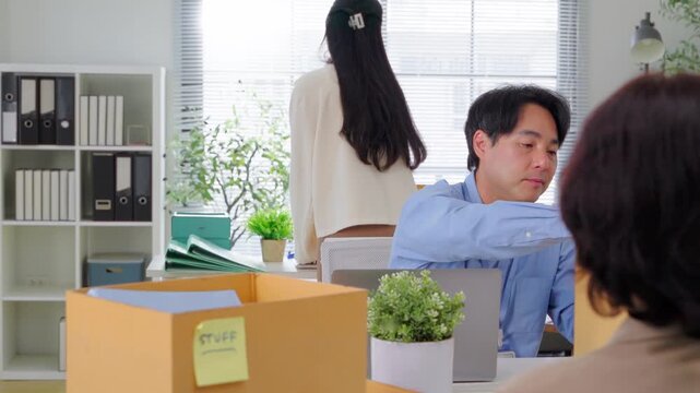 A businessman takes off his employee lanyard and ID badge while standing over a cardboard box, packing up his desk in a modern office, symbolizing job termination and career transition.