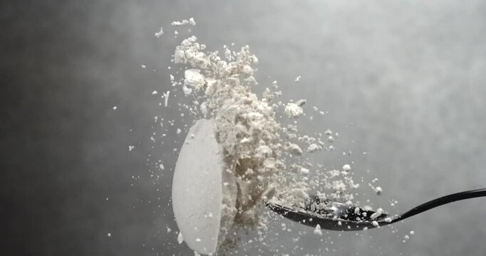 Flour falling from black spoon in super slow motion