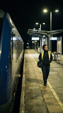 Frau in Warnweste geht nachts allein &uuml;ber den menschenleeren Bahnsteig neben einem blauen Zug