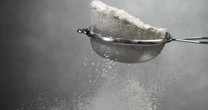 Flour sifts through a sieve creating soft powder cloud in slow motion