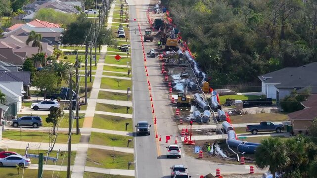 Aerial view of roadwork zone in Florida, showing pipe-laying operation near homes, traffic diverted by cones and construction vehicles.