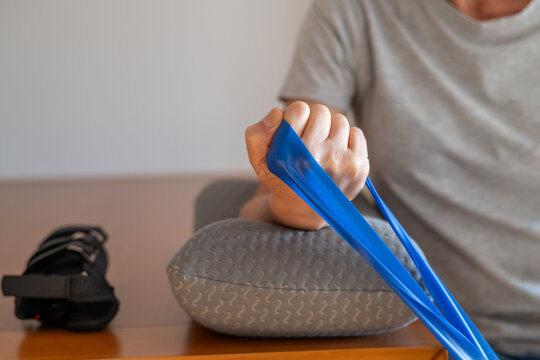 Person doing physical therapy using a blue resistance band to strengthen hand and arm muscles, aiding in rehabilitation and recovery from wrist injuries like carpal tunnel or tendinitis
