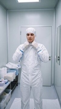 Junger Mann im wei&szlig;en Reinraumanzug zieht konzentriert die Kapuze in einer sauberen Schleuse einer Chipfabrik an