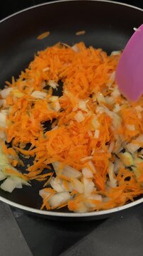 Close up of stirring grated carrots and chopped onions saut&eacute;ing in a hot frying pan.