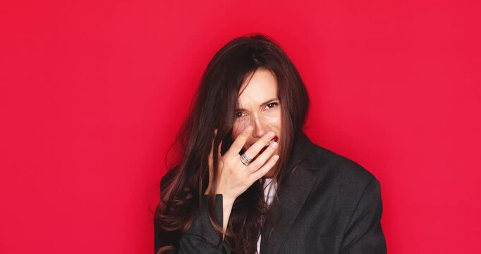 Stressed young woman with long dark hair and red lipstick covering face with hand feeling embarrassed and disappointed with a negative grimace expression isolated on a solid red studio background