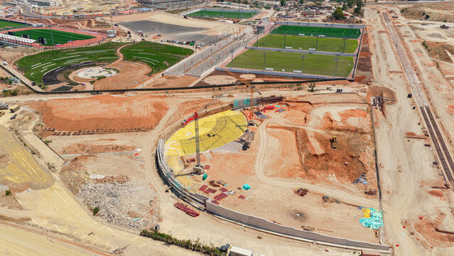 Developing sports complex showcasing an ongoing stadium construction site with cranes. Earthwork. And multiple finished and partially built sports fields. Representing progress in urban infrastructure