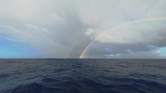Double rainbow over the dark blue ocean water under a cloudy sky