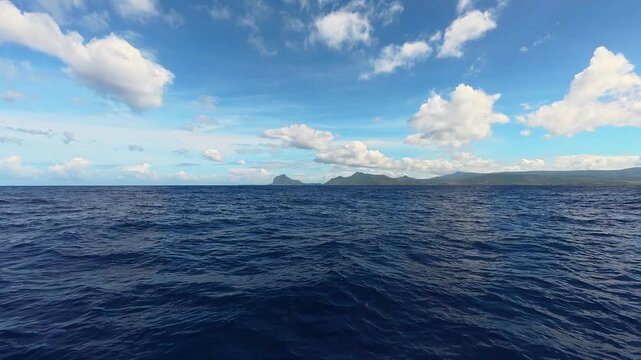 Scenic view of the deep blue ocean with distant mountains on the horizon under a bright sunny sky with clouds