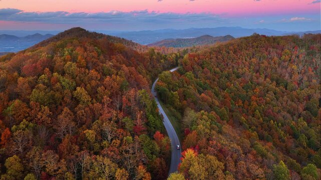 Car driving along mountain road in evening surrounded by colorful autumn trees in Tennessee. Scenic road trip through the Appalachians in fall season.