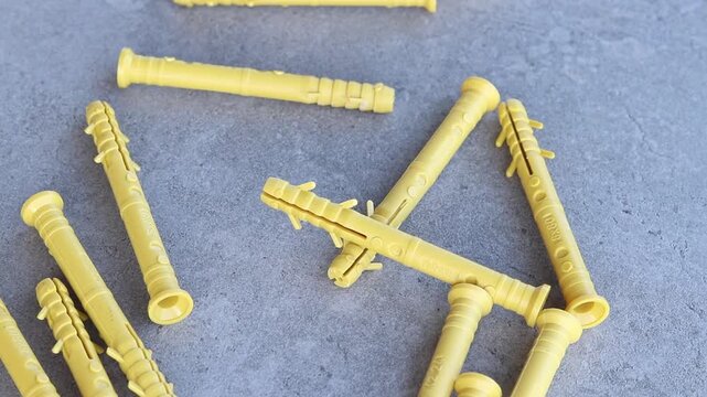Yellow dowels for installation and construction are scattered on a gray concrete background. Construction fasteners. Yellow expansion dowels for quick installation are spilled out on a gray surface