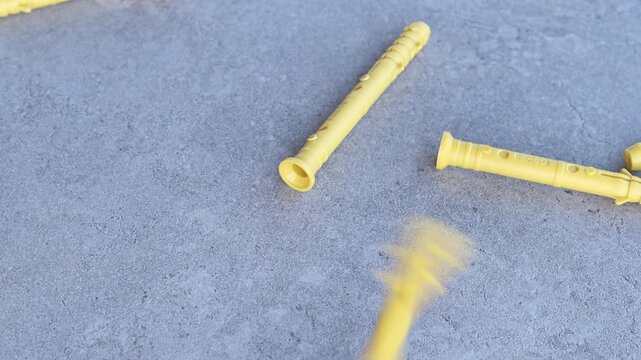 Yellow dowels for installation and construction are scattered on a gray concrete background. Construction fasteners. Yellow expansion dowels for quick installation are spilled out on a gray surface