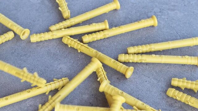 Yellow dowels for installation and construction are scattered on a gray concrete background. Construction fasteners. Yellow expansion dowels for quick installation are spilled out on a gray surface