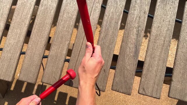 A man plays a wooden xylophone in the park with rubber red mallets. Natural musical instrument for adults and children. High quality 4k footage