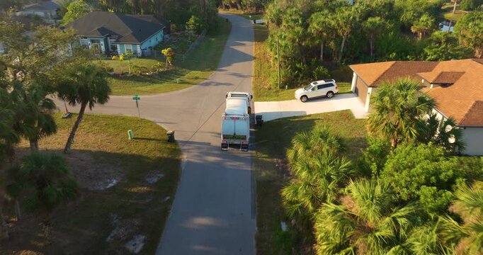 Garbage removal in residential area. Waste truck loading household rubbish while driving on suburban street.