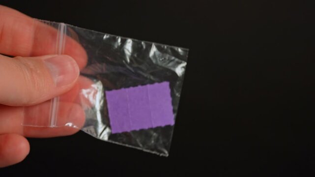 Drug dealer with LSD acid paper squares packed in small bag for sale, controlled drugs. Hallucinogenic psychedelic substances used in party and dance clubs.