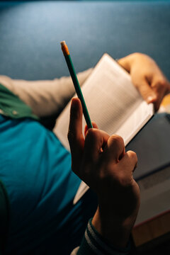 Person holding pencil, paused in thought or taking notes, while engaged in deep study with an open book, concept of dedication to learning and education..