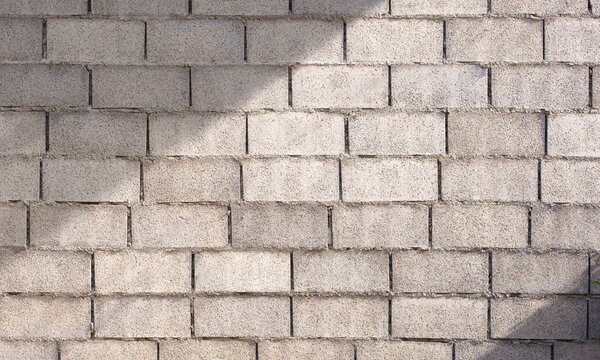 Concrete block wall background with natural sunlight and shadow, rough texture for construction backdrop design.